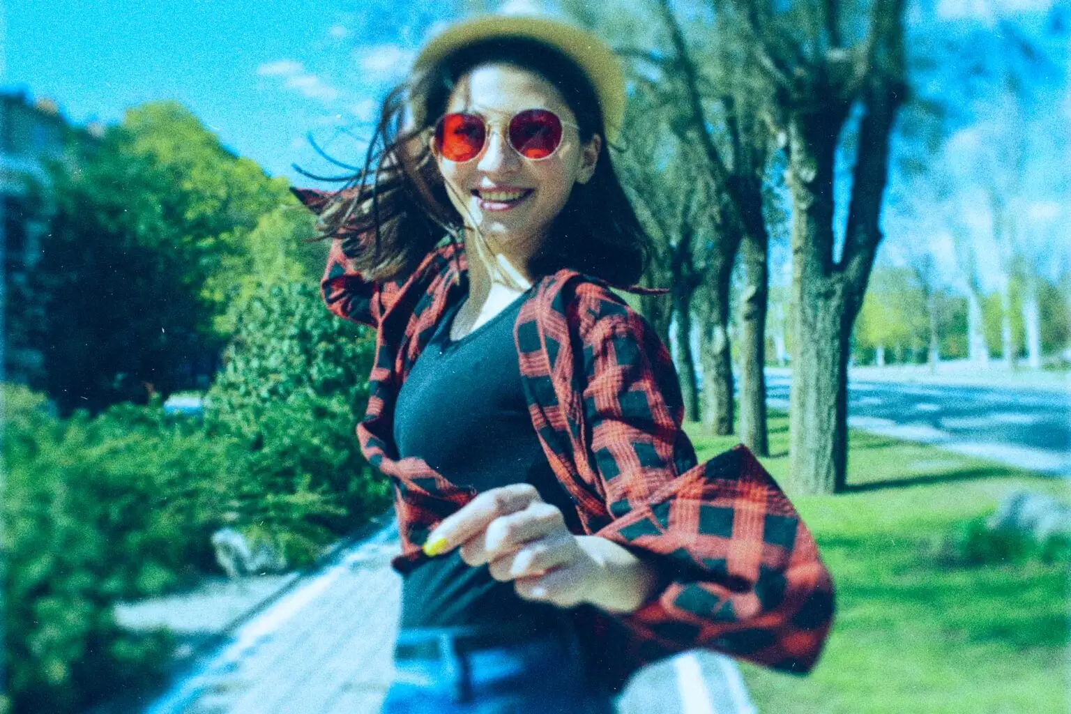 girl twirling with red and black flannel shirt and red-colored sunglasses and a beige sun hat