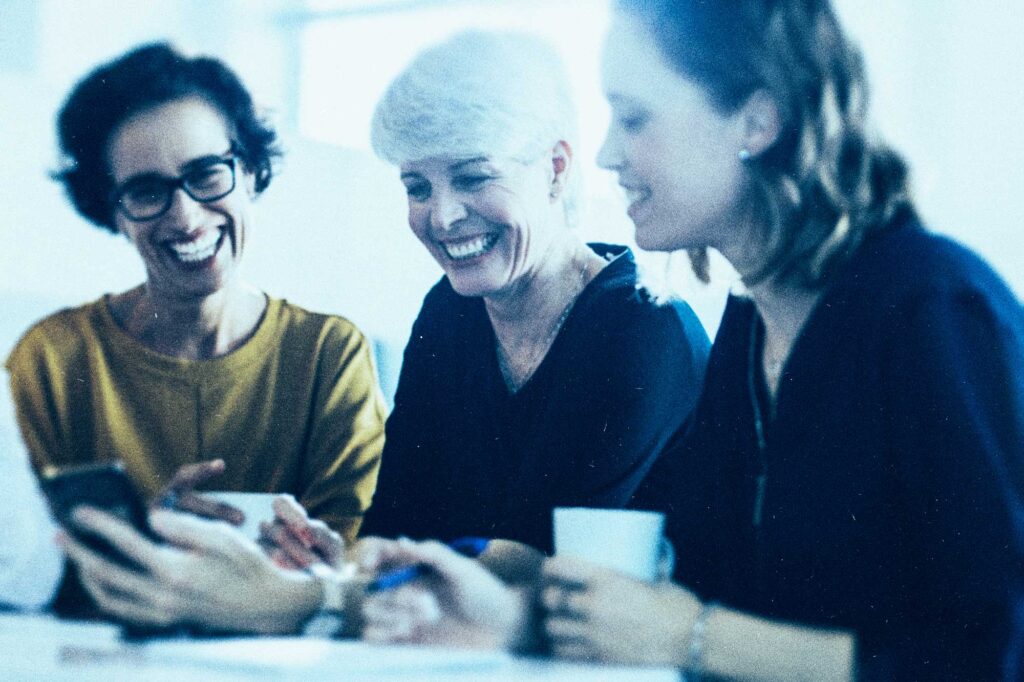 ladies gathered with coffee and smiling with a window behind them and sunlight coming in